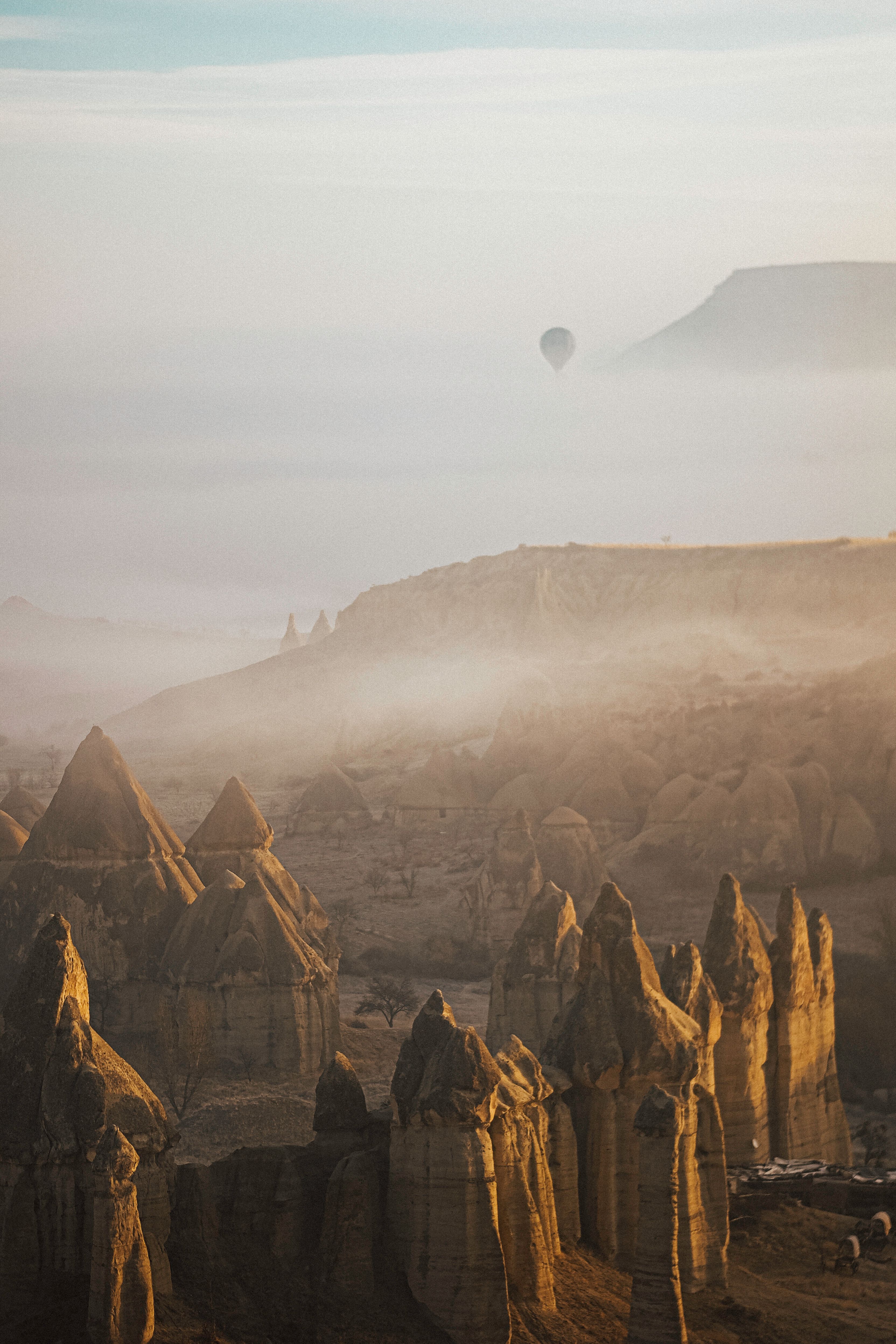 Scenic view of Cappadocia's rock formations and a distant hot air balloon in the mist.