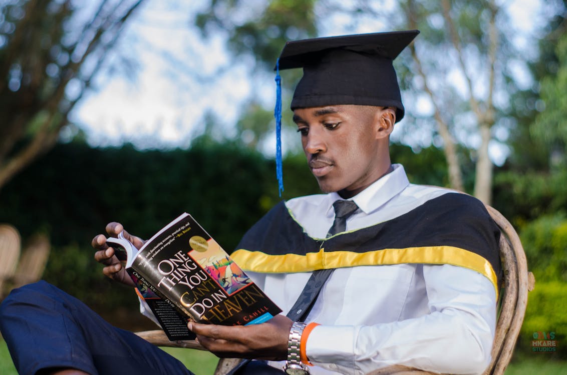 Person reading a book with a graduation cap nearby Person reading a book with a graduation cap nearby