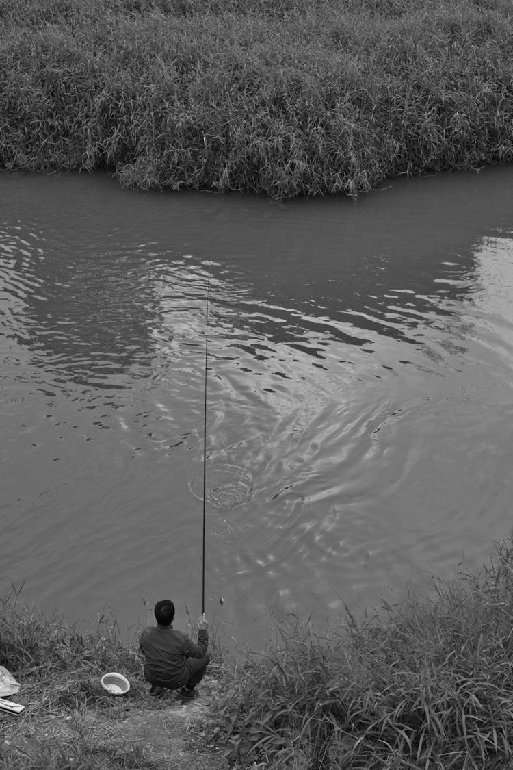 Grayscale Photo Of A Man Fishing On The River