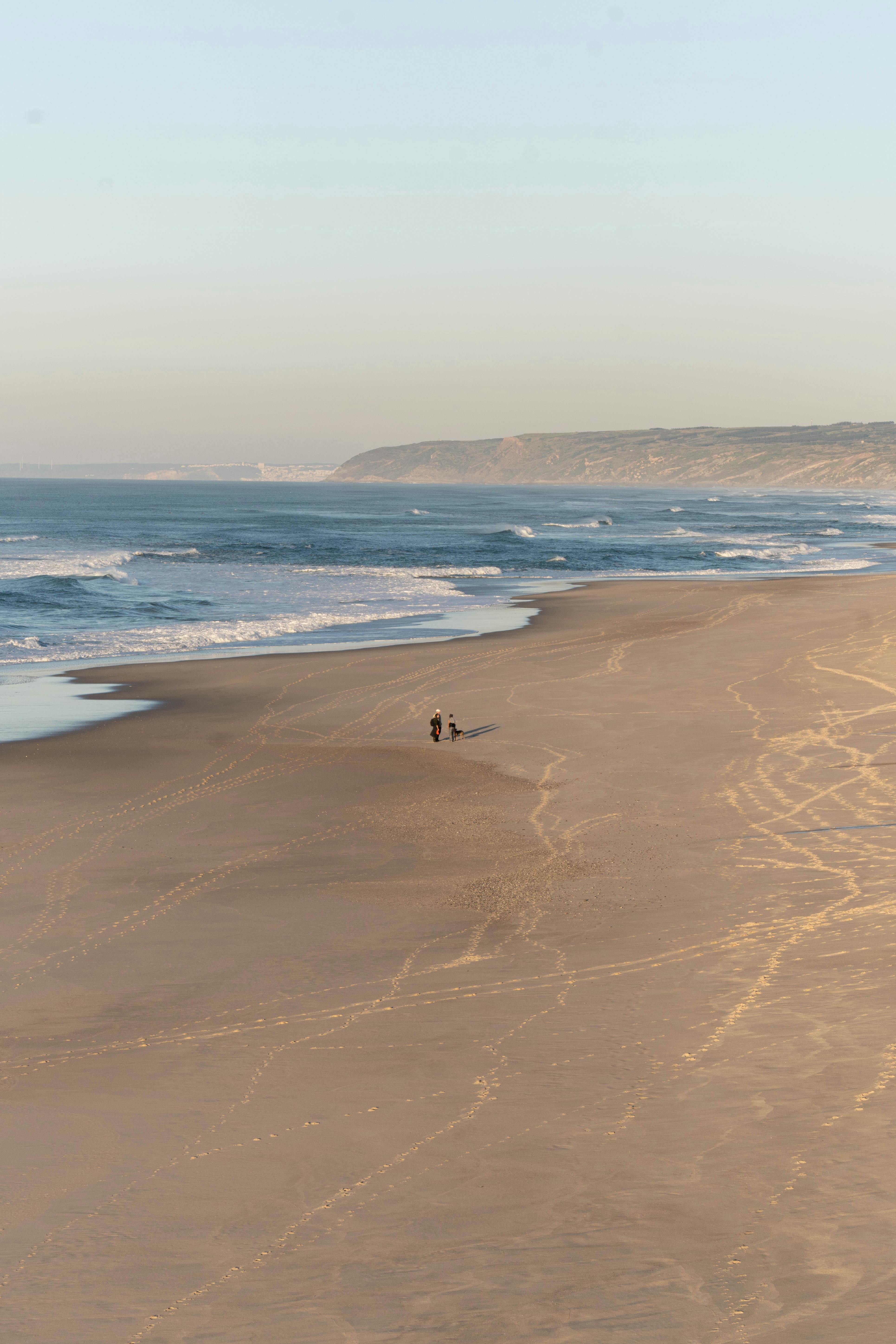 Serene aerial view of a couple walking on the expansive Nazaré Beach, Portugal.