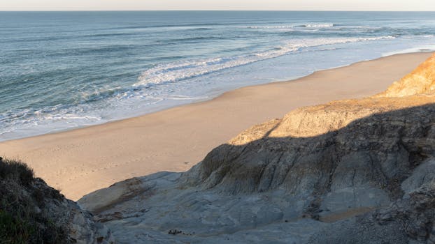 Peaceful beach scene with crashing waves at Nazaré, Portugal, during daytime.