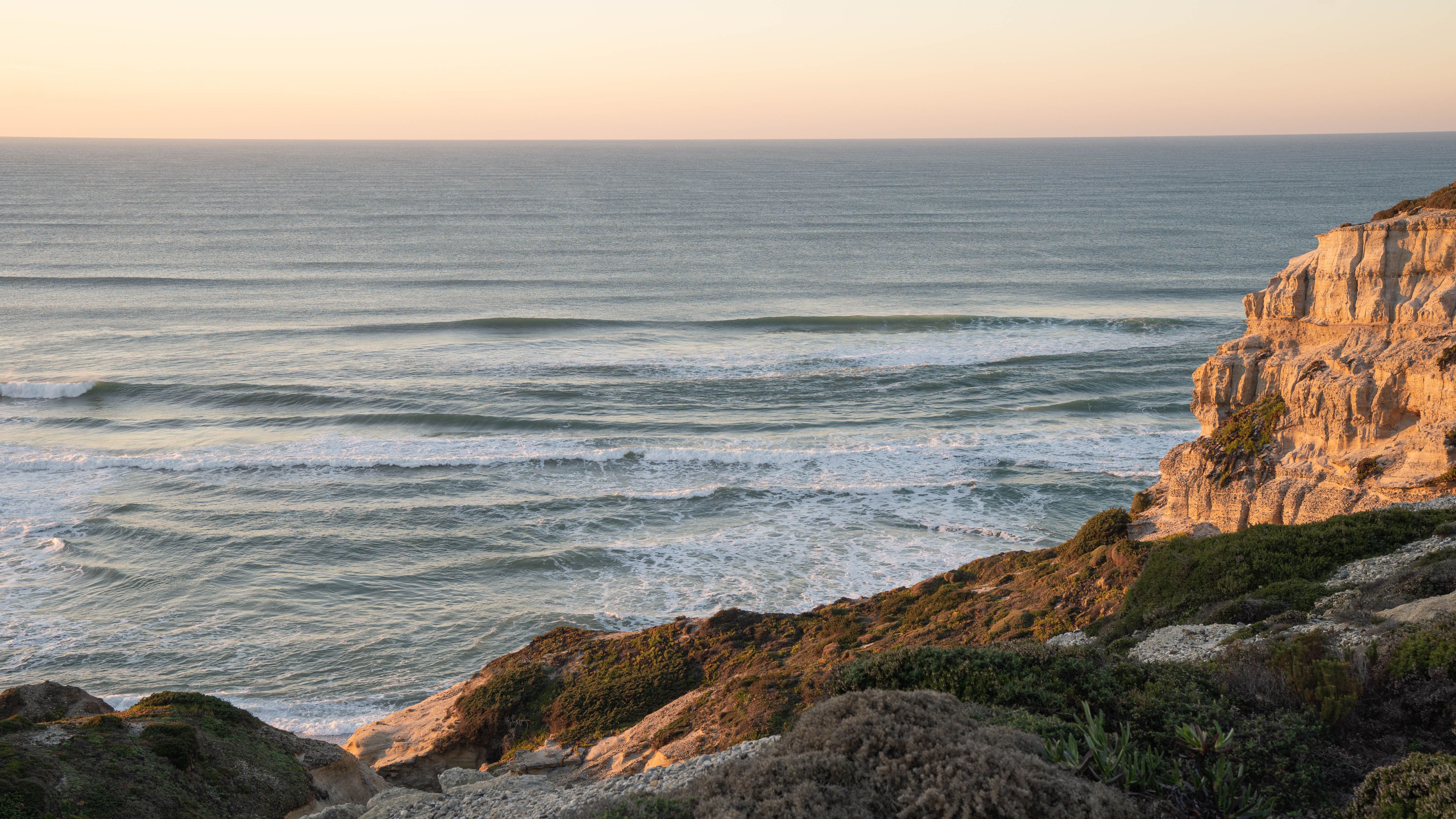 Golden hour view of the ocean and cliffs in Nazaré, Portugal, capturing the serene coastal landscape.