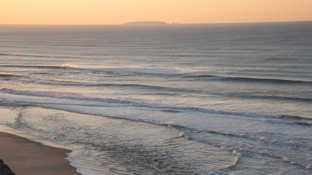 Beautiful sunrise at the beach in Nazaré, Portugal with serene ocean waves and a golden sky.