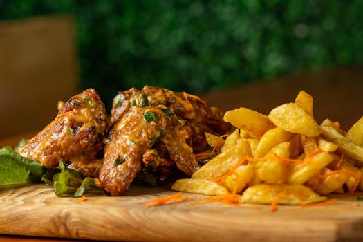 Appetizing close-up of fried chicken wings and crispy fries on wooden board.