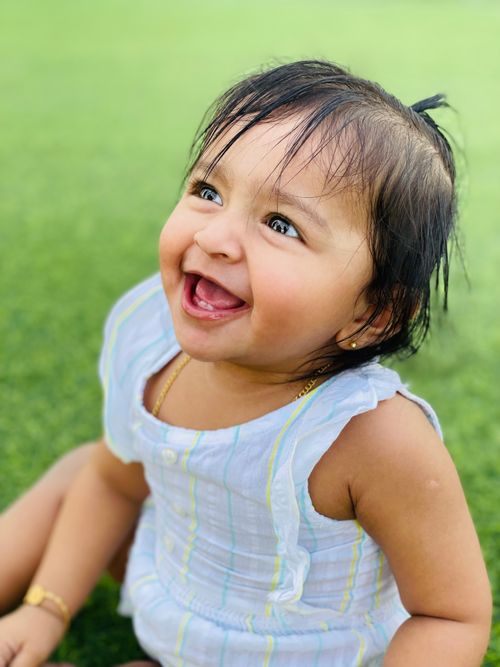 Free Charming portrait of a smiling baby sitting on green grass, enjoying a sunny day outdoors. Stock Photo