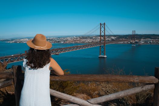 Woman admiring the iconic 25 de Abril Bridge in Lisbon from a viewpoint on a sunny day.