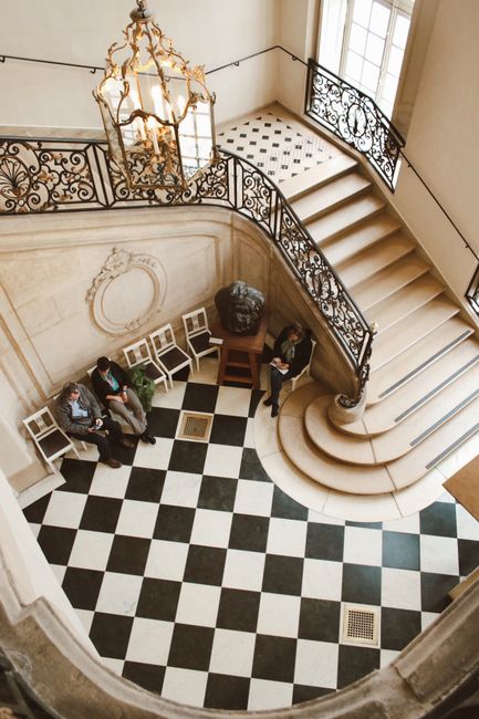Elegant lobby with black and white checkered floor and ornate staircase viewed from above.
