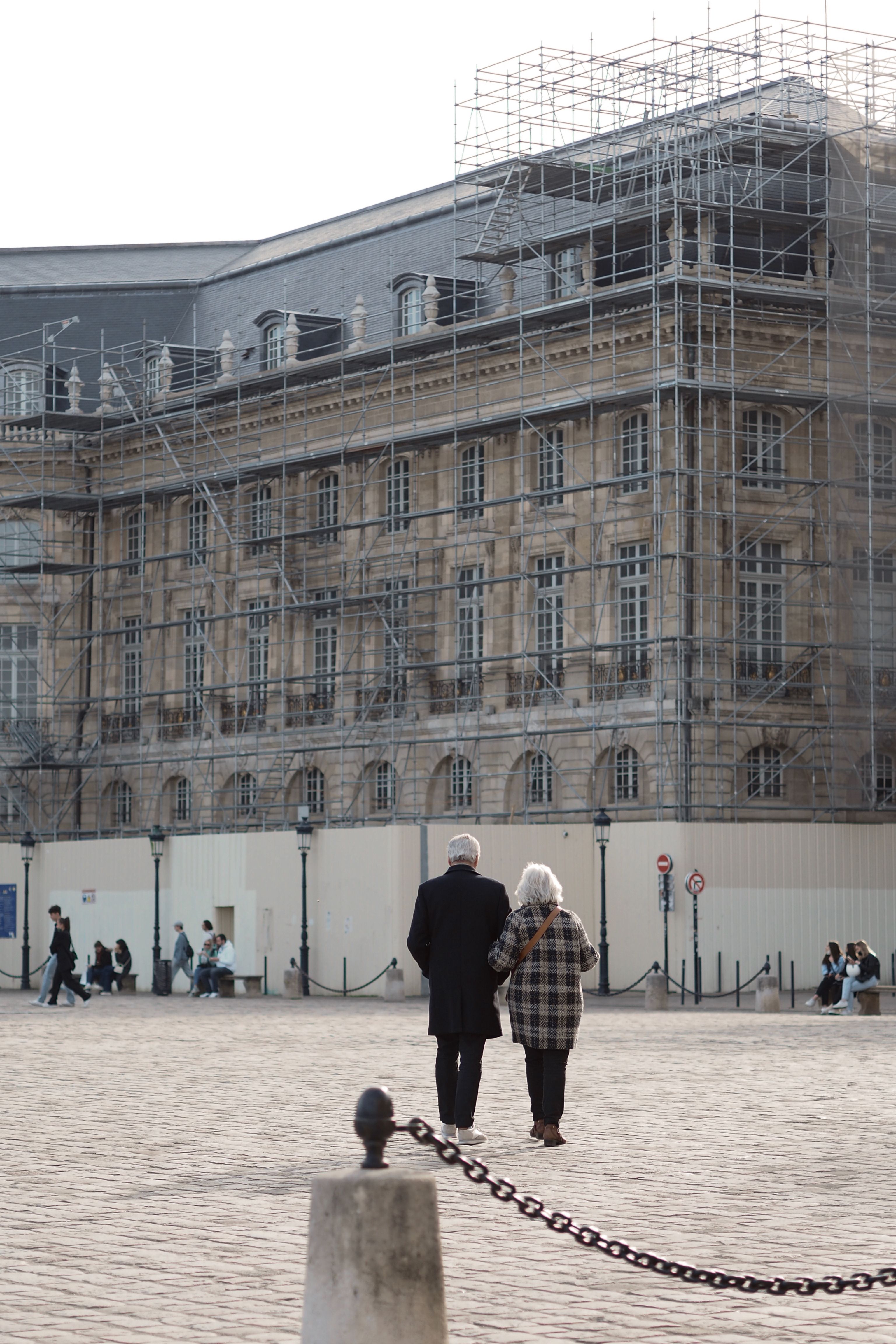 Elderly couple walking near a historic building under renovation, showcasing urban lifestyle.