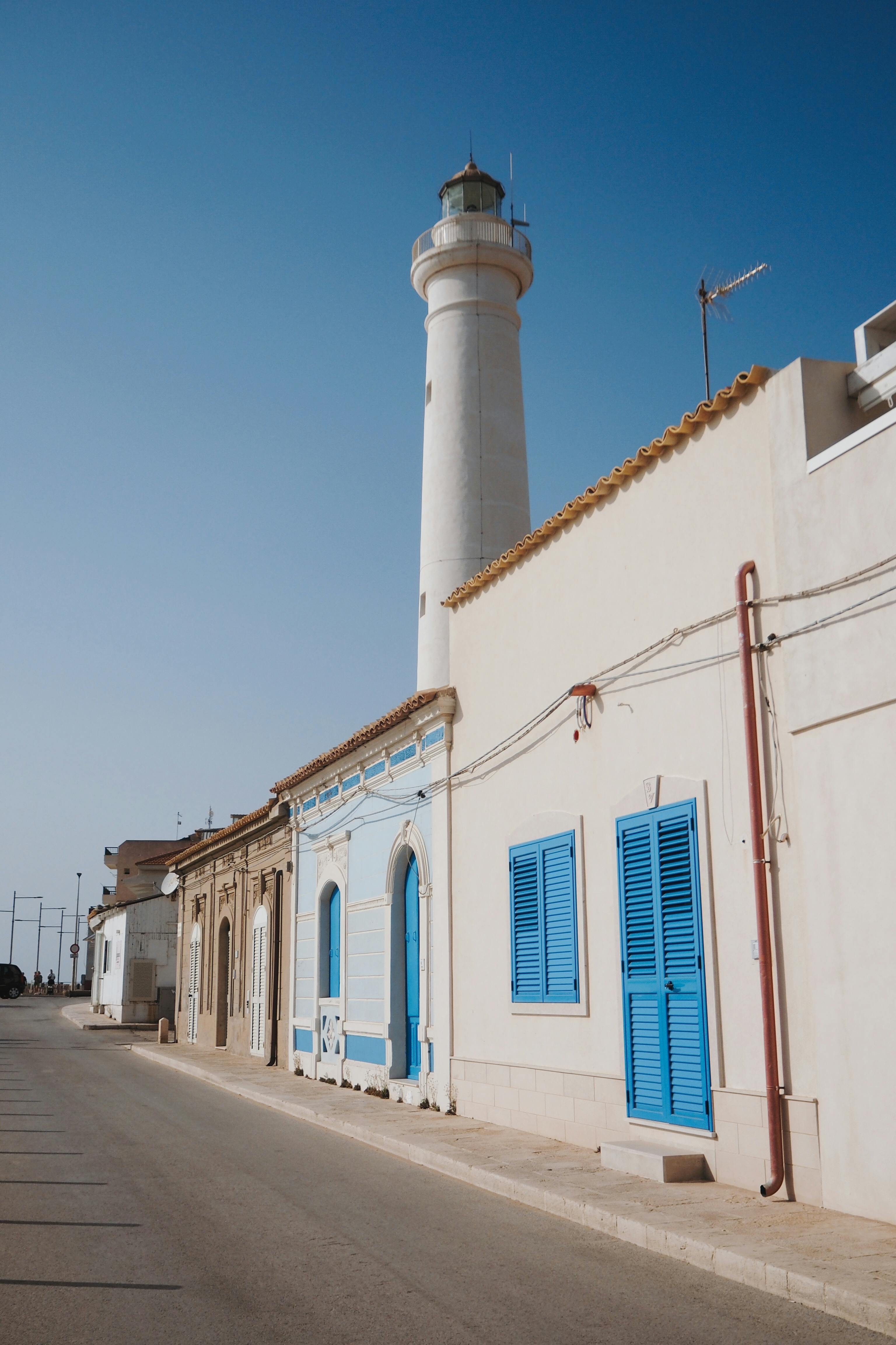 Bright blue sky over a charming Sicilian street with a lighthouse and colorful houses.