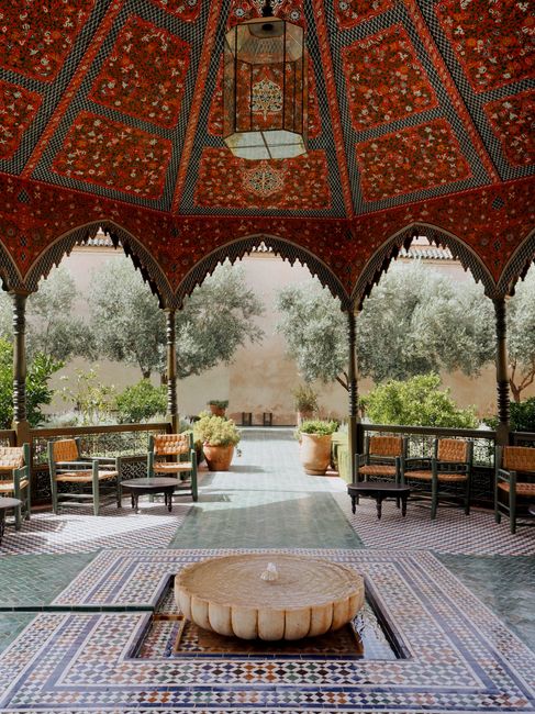 Sophisticated patio with mosaic decor, elegant chairs, and a central fountain under an ornate canopy.