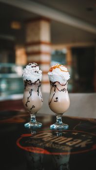 Indulgent milkshakes adorned with whipped cream and drizzled toppings on a cafe table.