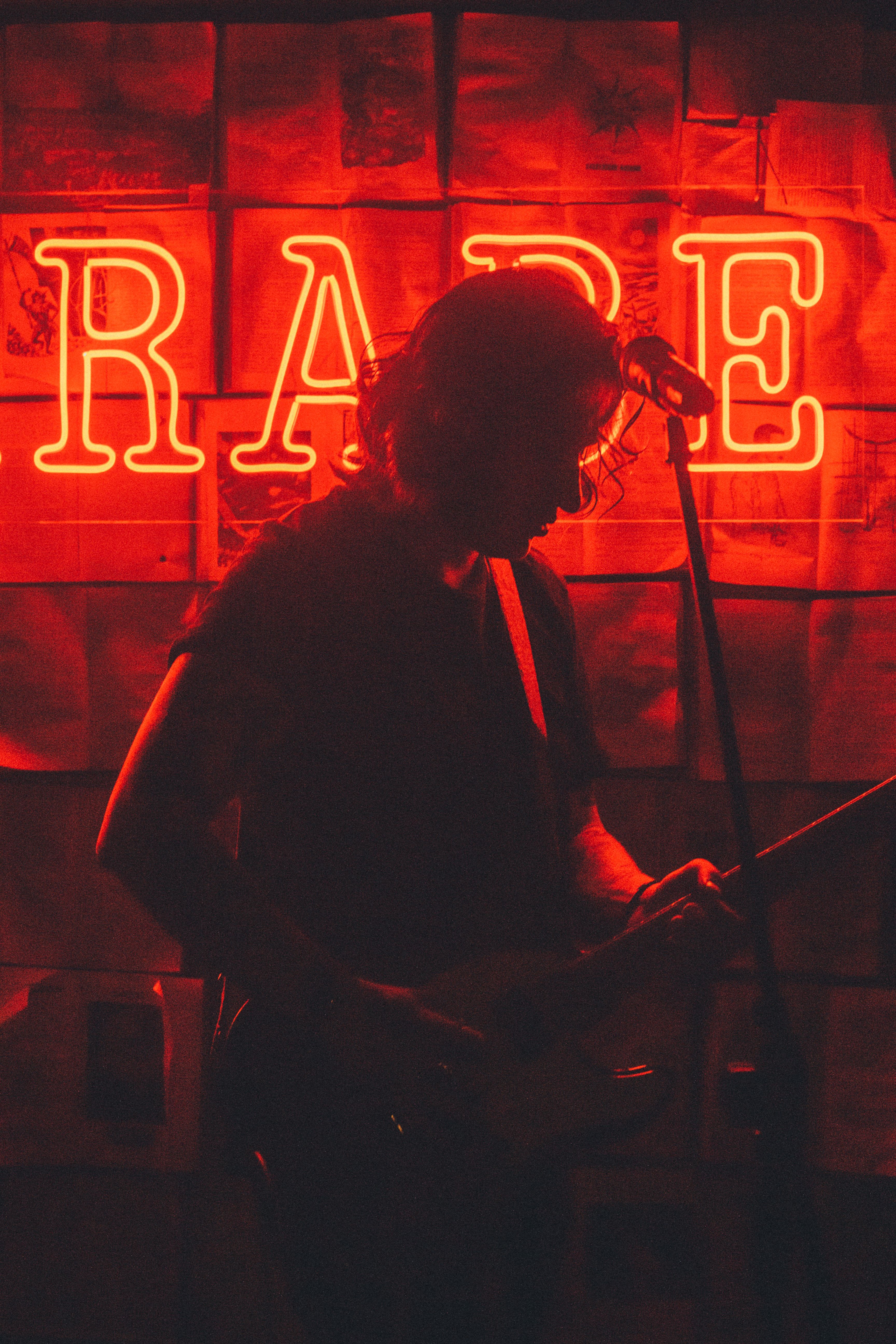 A captivating silhouette of a musician playing guitar under red neon lighting on stage.
