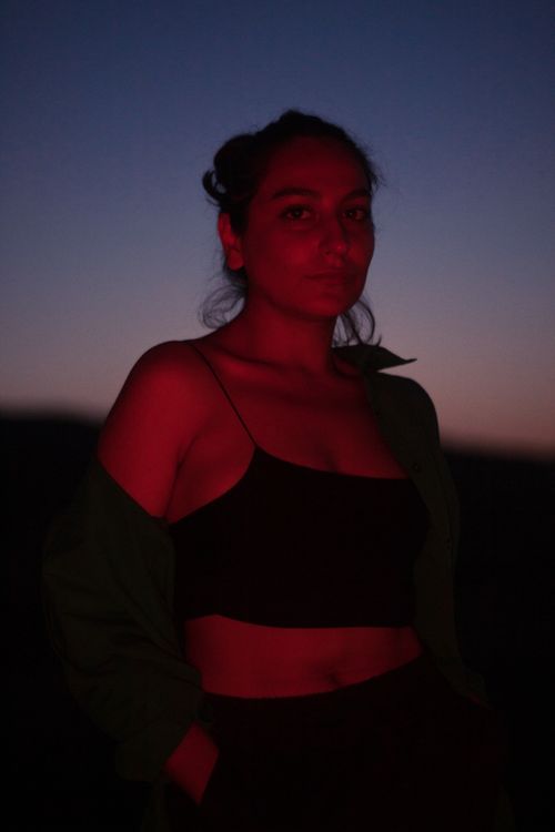 Free Emotive portrait of a woman standing under a clear dusk sky, lit with dramatic red lighting. Stock Photo