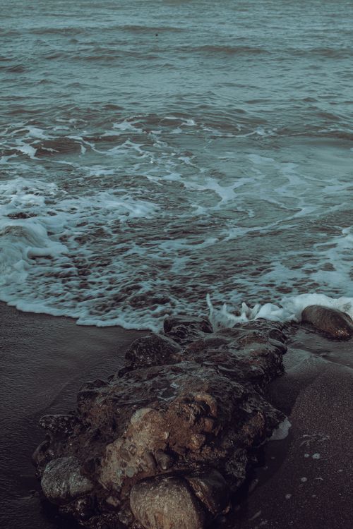 Free Peaceful beach scene with rocks and gentle waves under the soft light, perfect for relaxation themes. Stock Photo