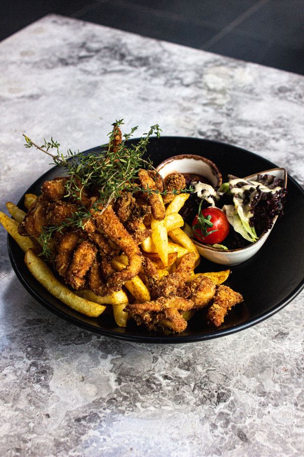 Um prato saboroso de frango frito com batatas fritas e salada em um prato preto, perfeito para amantes da comida.