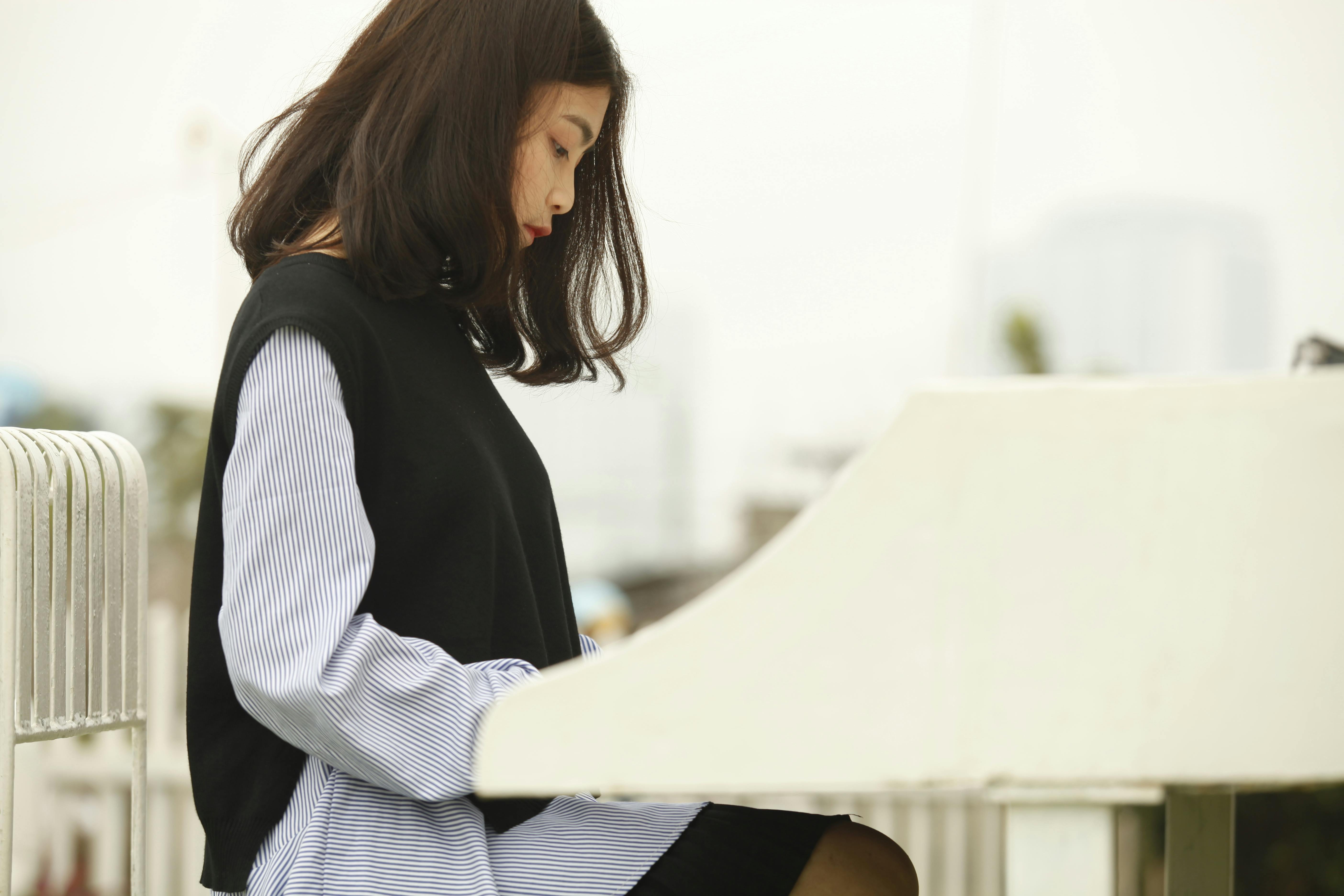 Profile of a young woman sitting at a piano outdoors, lost in thought.