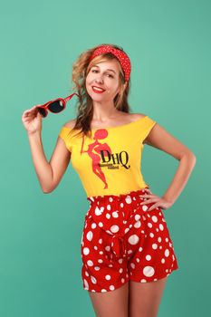 Smiling woman in vintage polka dot attire posing with sunglasses in a studio setting.