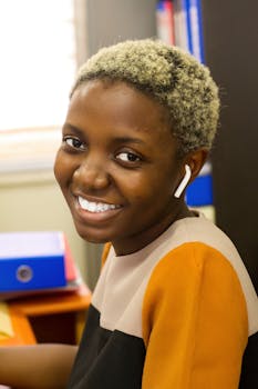 Happy black woman with short curly blonde hair and wireless earbuds smiling in an office setting.