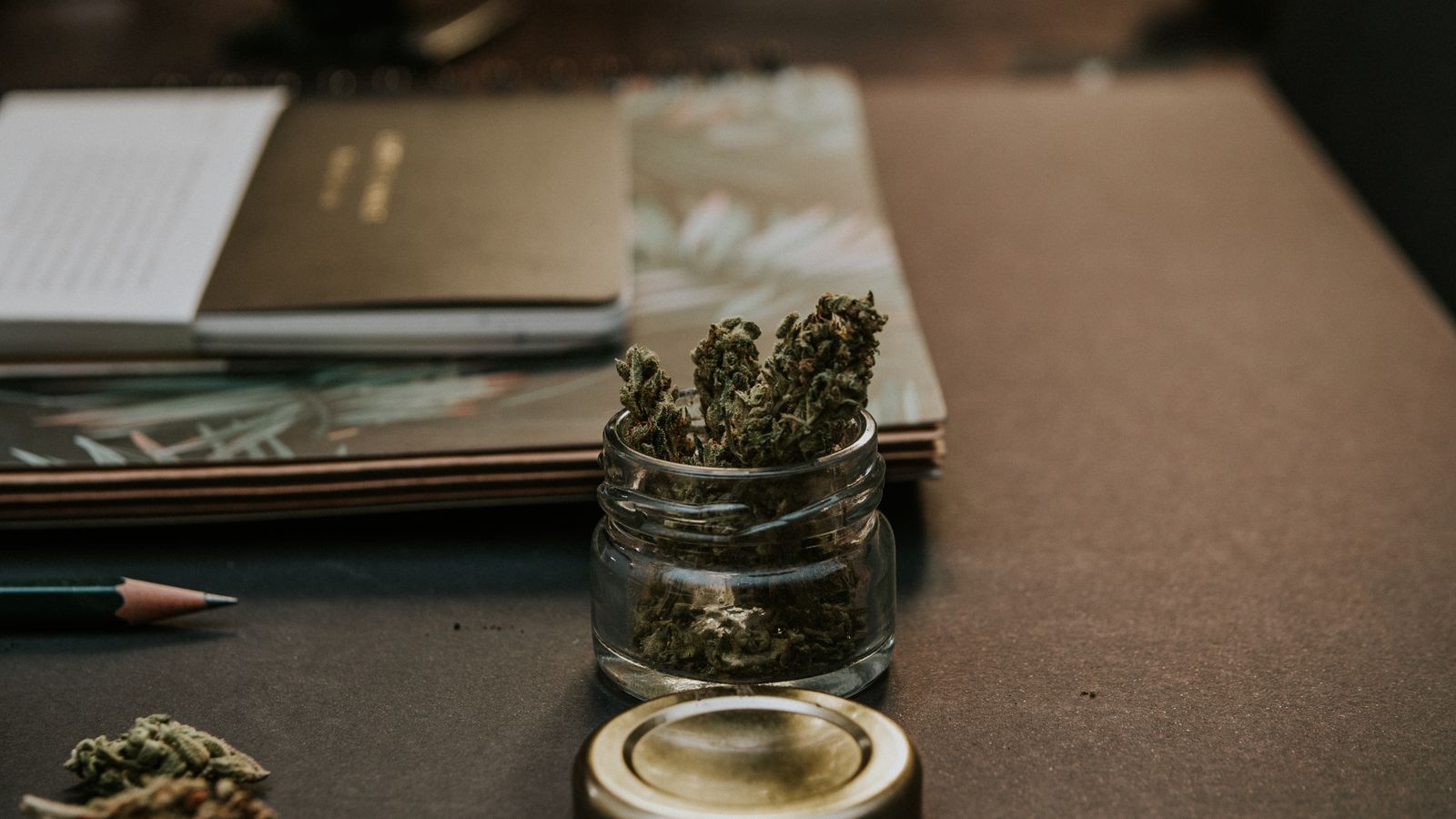 A close-up image of cannabis buds in a glass container on a desk, emphasizing a natural and relaxed setting.