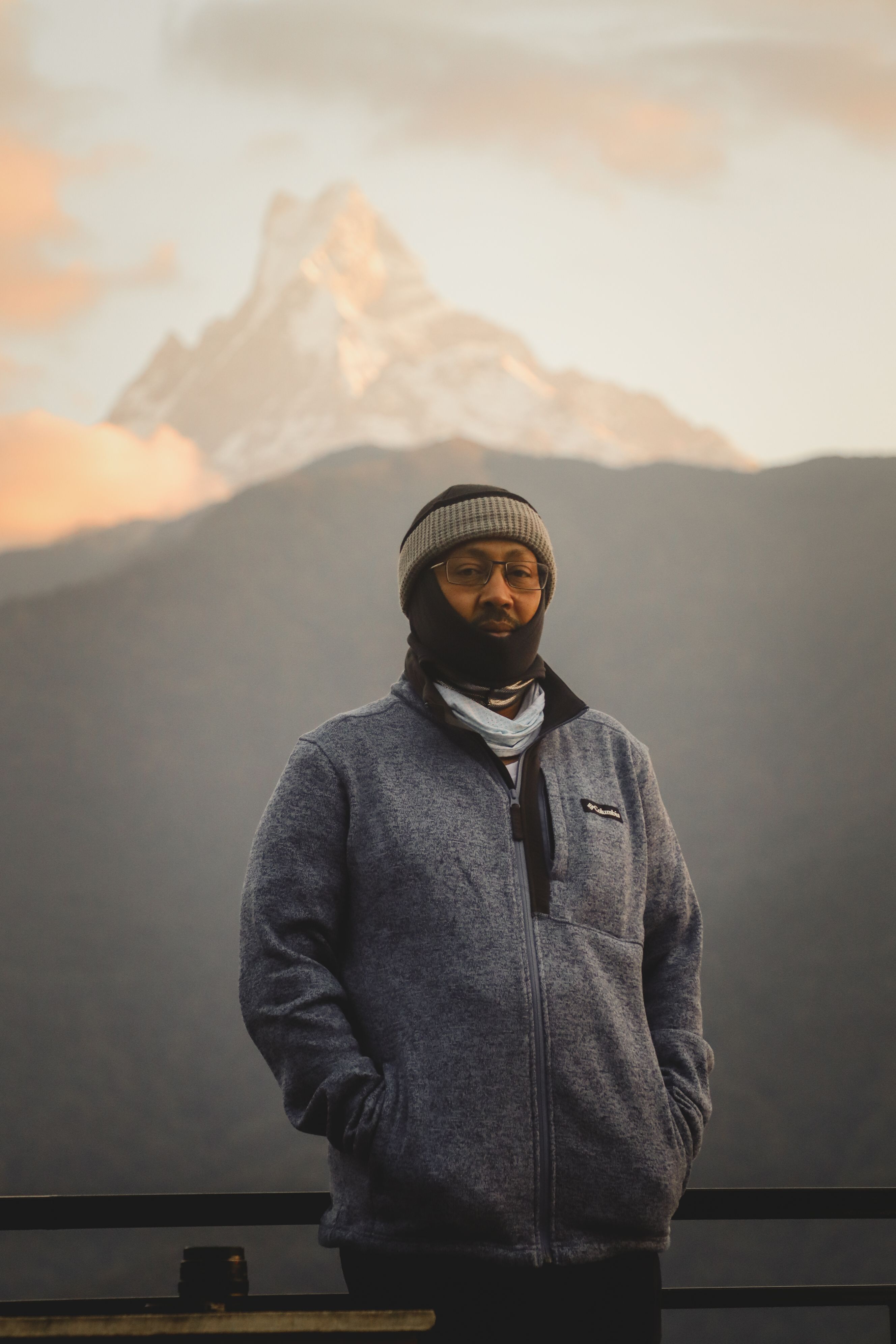 Man in Ghandruk, Nepal with the Himalayas in the background, wearing a gray jacket and beanie.