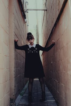 Moody urban portrait of a woman in a cat-themed dress in a narrow alleyway.