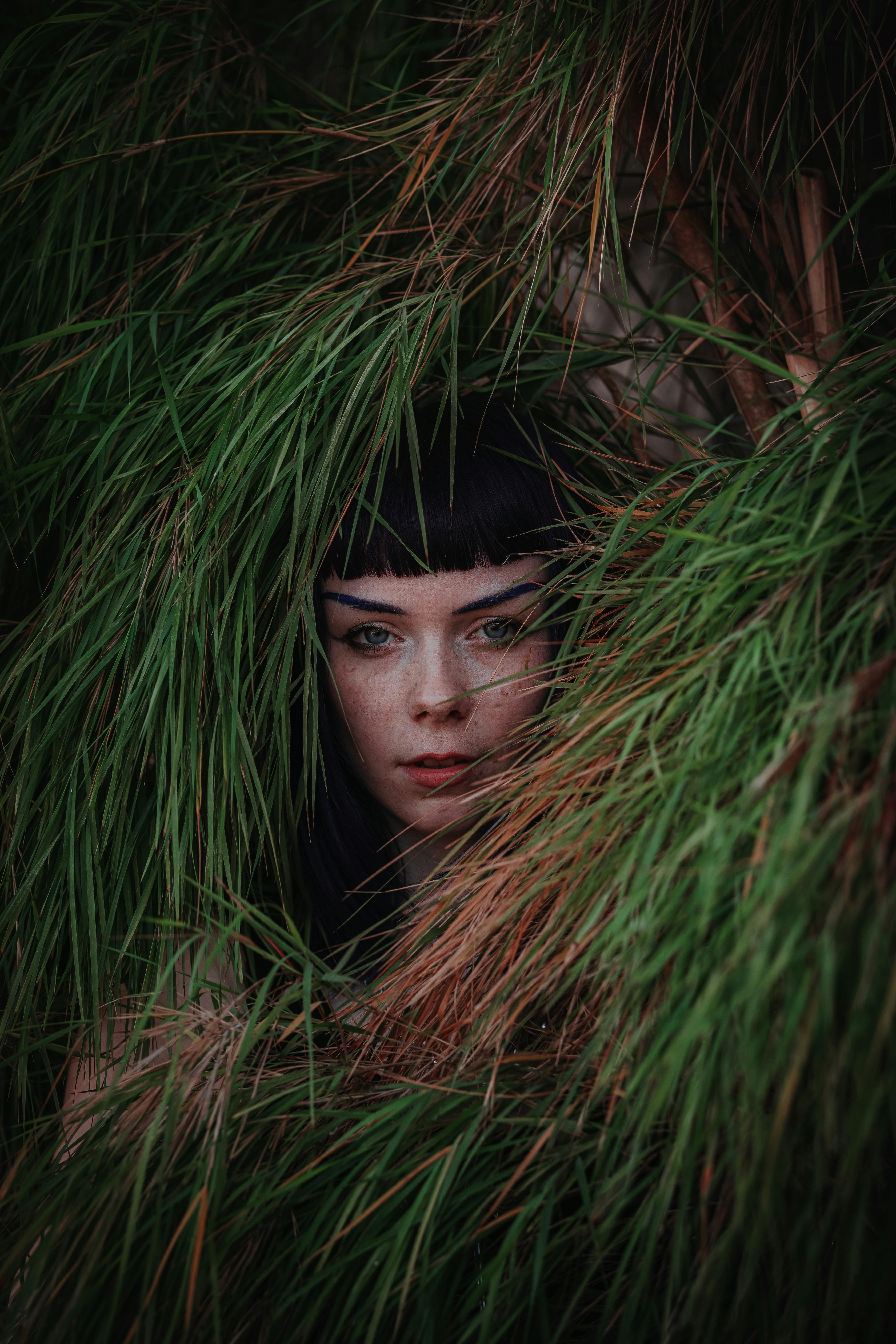 a woman with black hair hiding behind some green grass