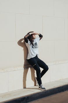 Young woman in casual attire leans against a wall in sunny Orlando, capturing urban style and mood.