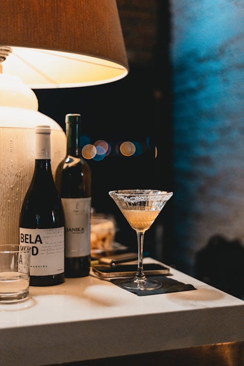 An Alcoholic Drink in a Cocktail Glass beside Bottles of Wine