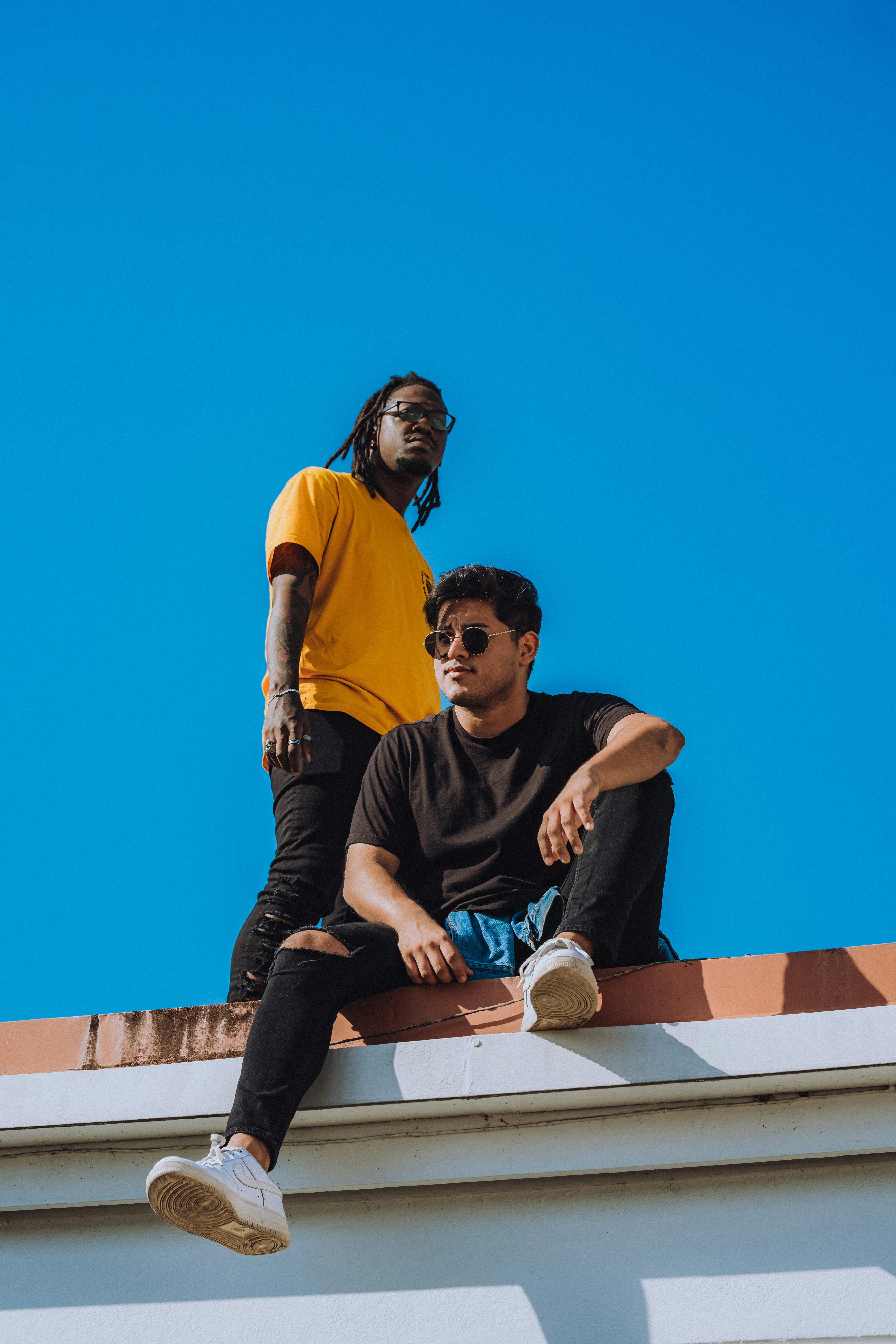 two men sitting on top of a roof with a blue sky in the background