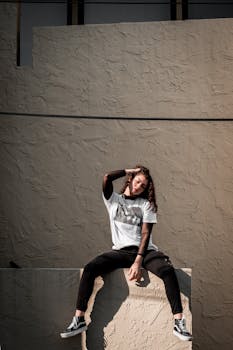A fashionable woman sitting on an urban wall, showcasing modern street style.