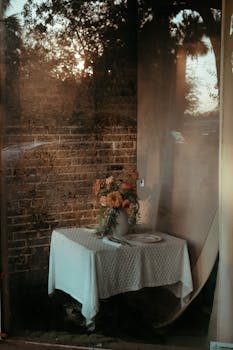 A cozy table with a floral arrangement set against a rustic brick wall at dusk.