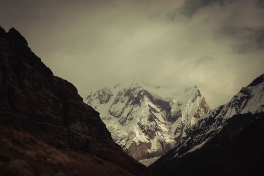 Dramatic view of snow-covered Annapurna mountain range under a cloudy sky in Nepal.