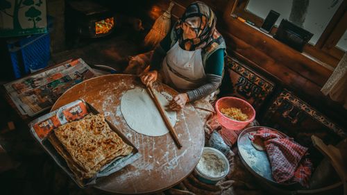 Free Elderly woman making homemade Turkish bread with a rolling pin in a cozy kitchen setting. Stock Photo