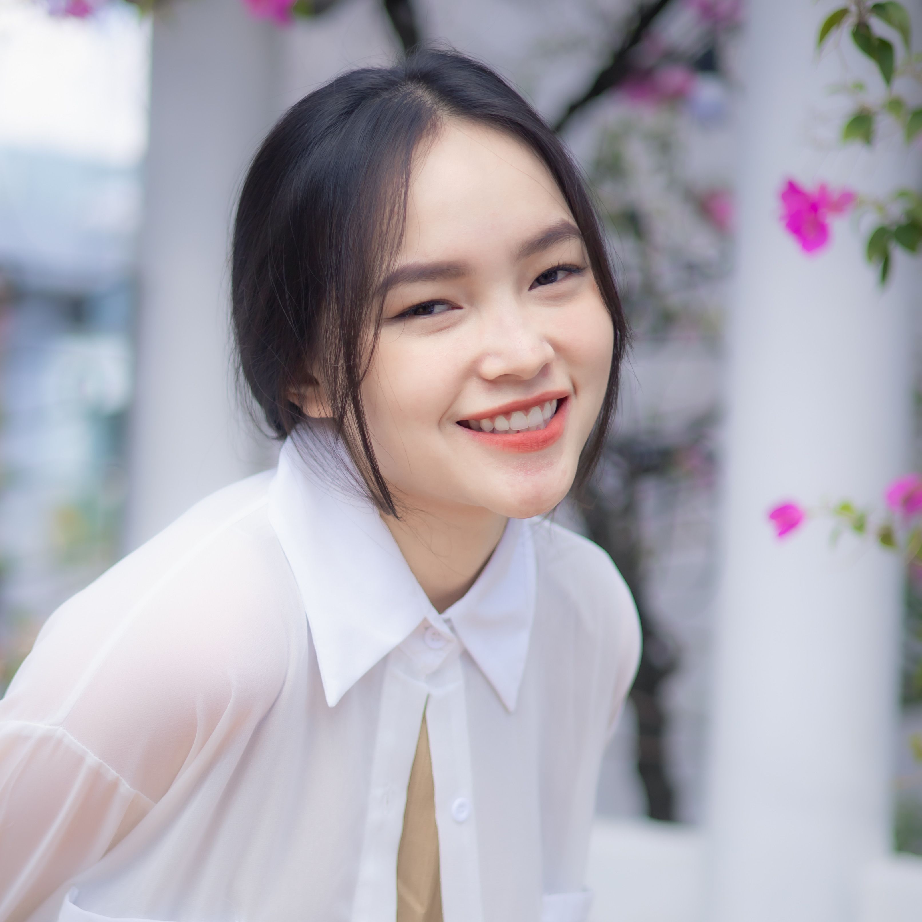 Cheerful young woman in a white blouse smiling in a vibrant garden setting in Ho Chi Minh City.