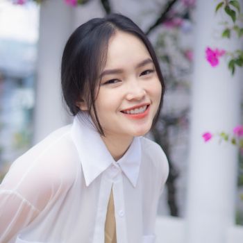 Cheerful young woman in a white blouse smiling in a vibrant garden setting in Ho Chi Minh City.