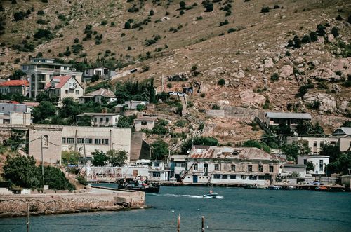 Free Charming coastal town nestled against a rugged hillside with boats and clear blue waters. Stock Photo