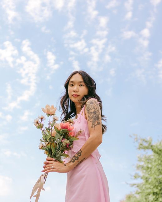 Elegant woman in pink dress holding flowers against a summer sky.