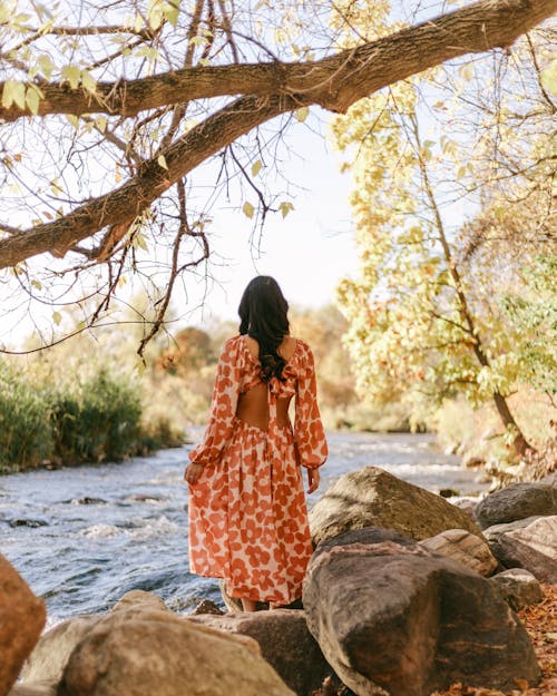 A Woman in Orange and White Floral Dress Standing Beside the River