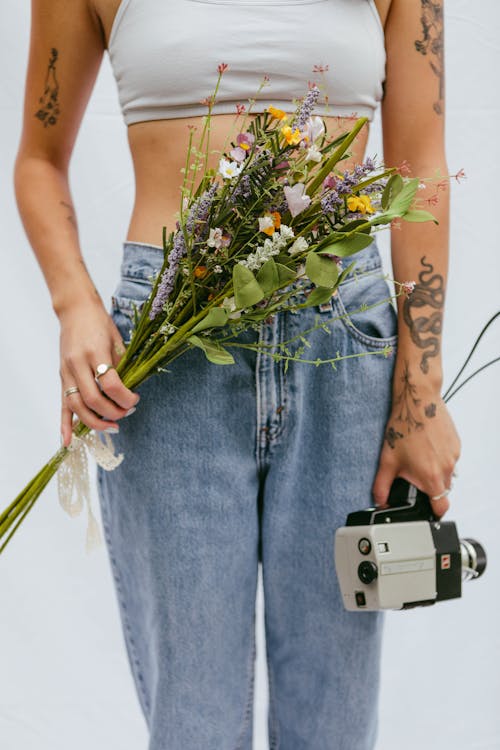 Woman in Jeans Holding Vintage Camera and Flowers