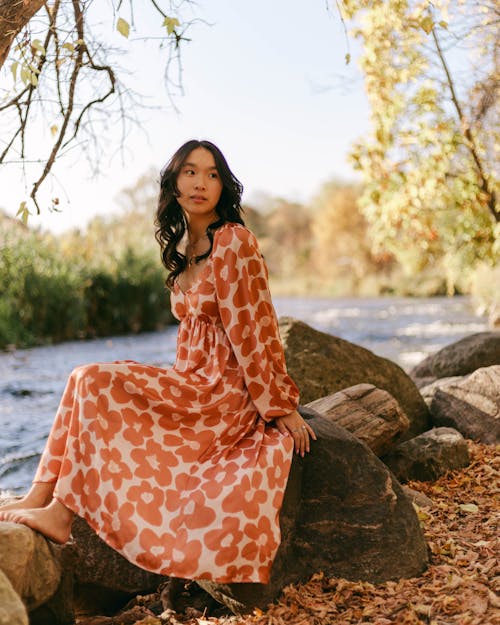 A Woman in Orange and White Floral Dress Sitting Beside the River