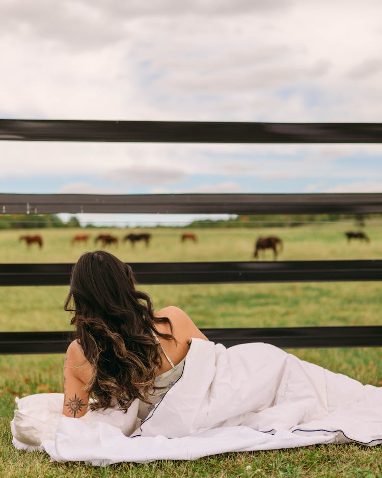 Woman Lying On Grass Against Pasture With Horses