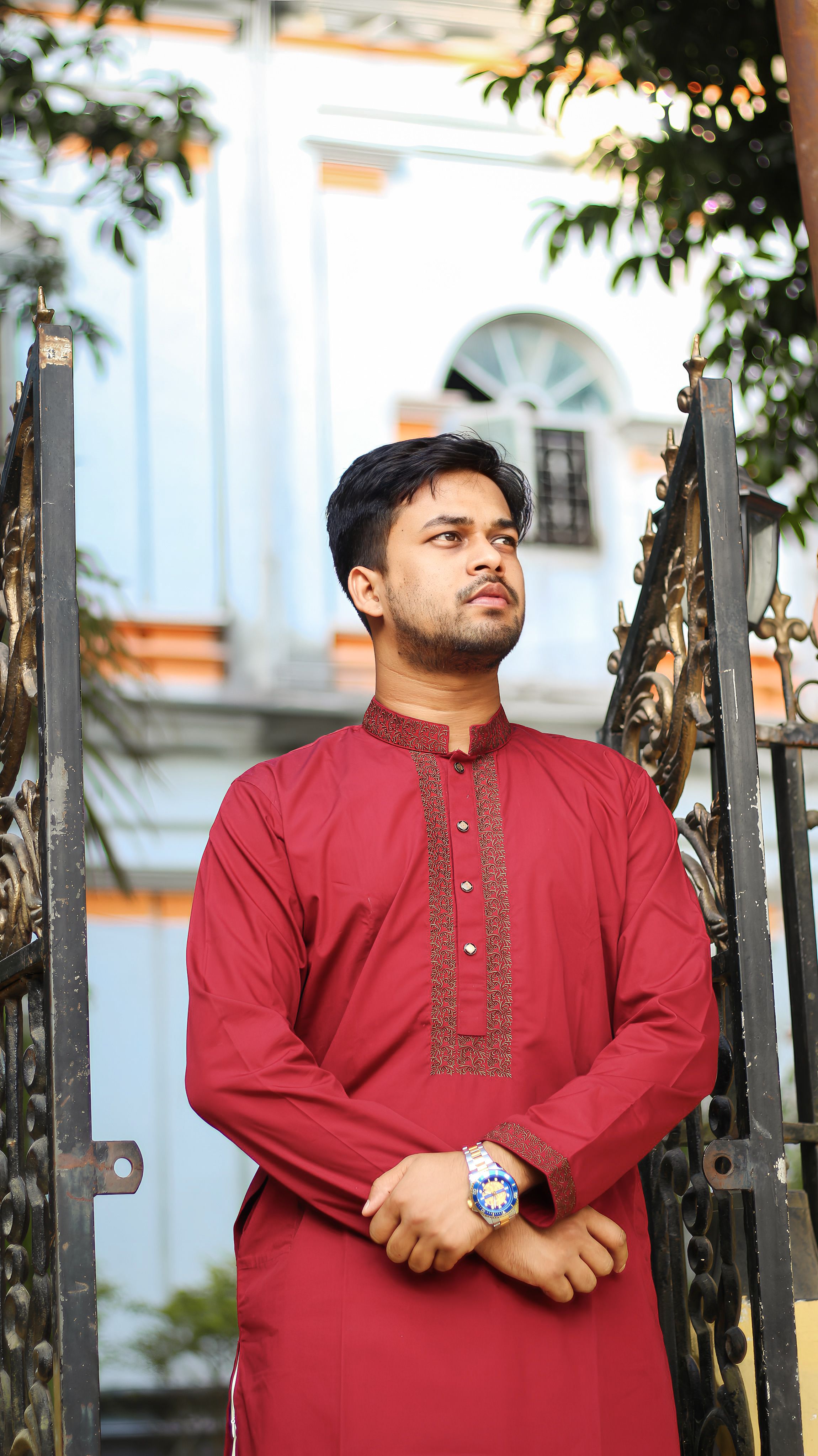 A confident man in a vibrant red kurta standing outdoors near a decorative gate, embracing tradition.