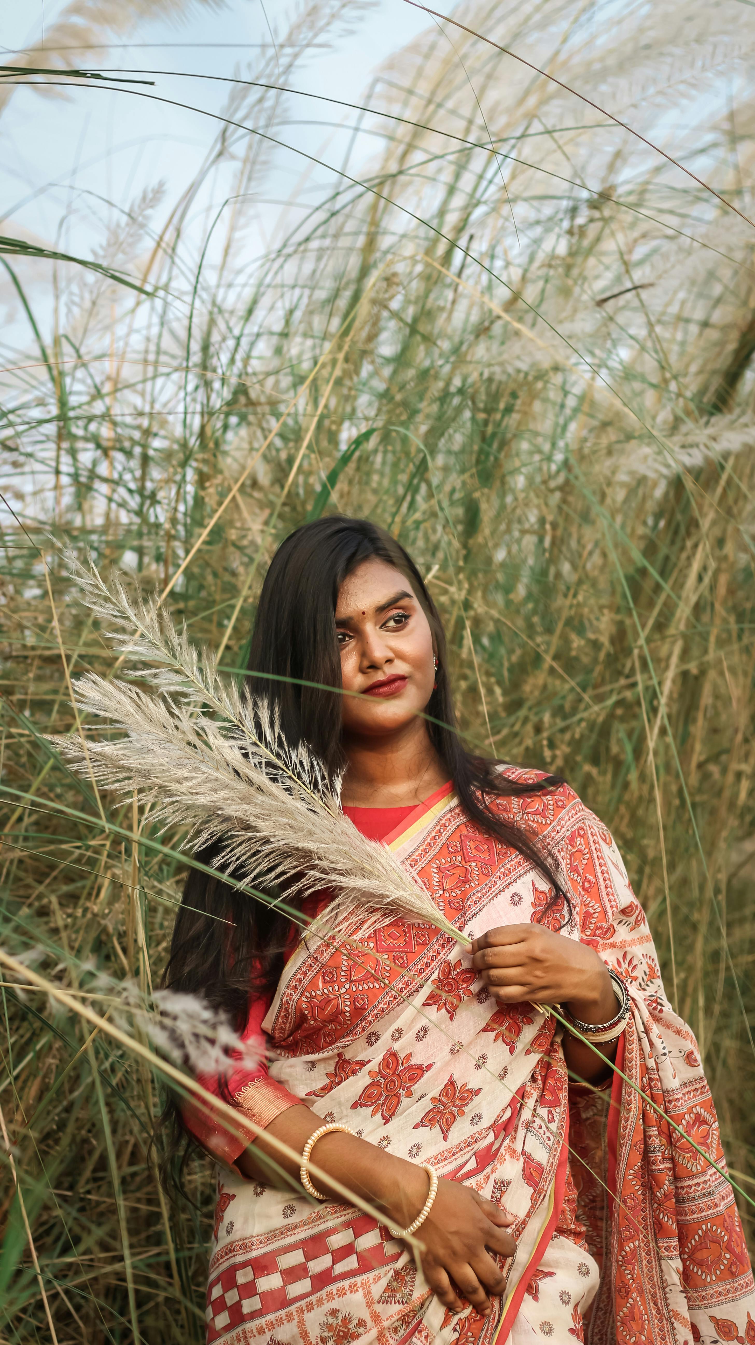 Portrait of a woman in a traditional saree posing gracefully in a field of tall reeds.