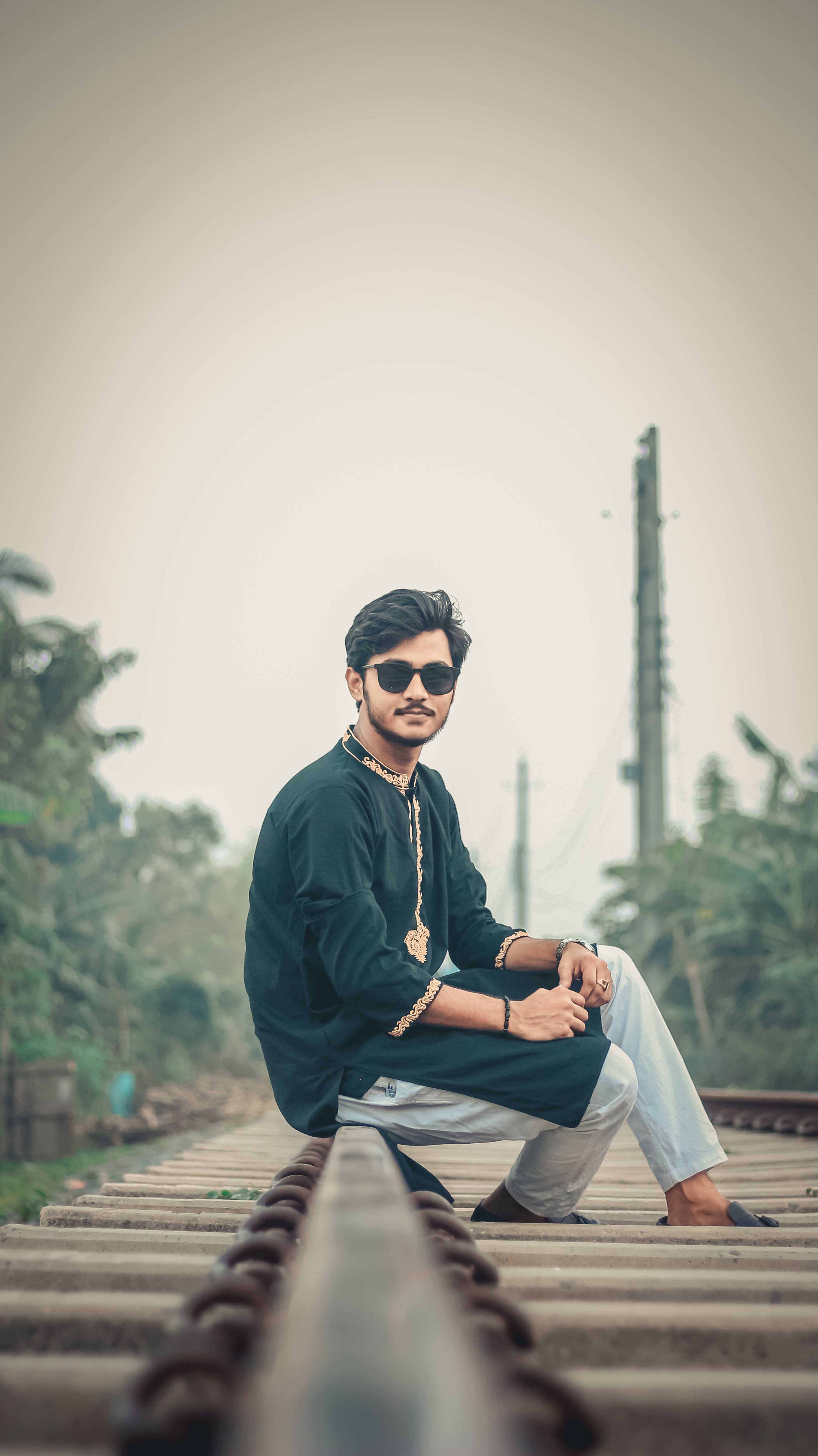 Fashionable man wearing sunglasses and kurta, sitting on a railway track.