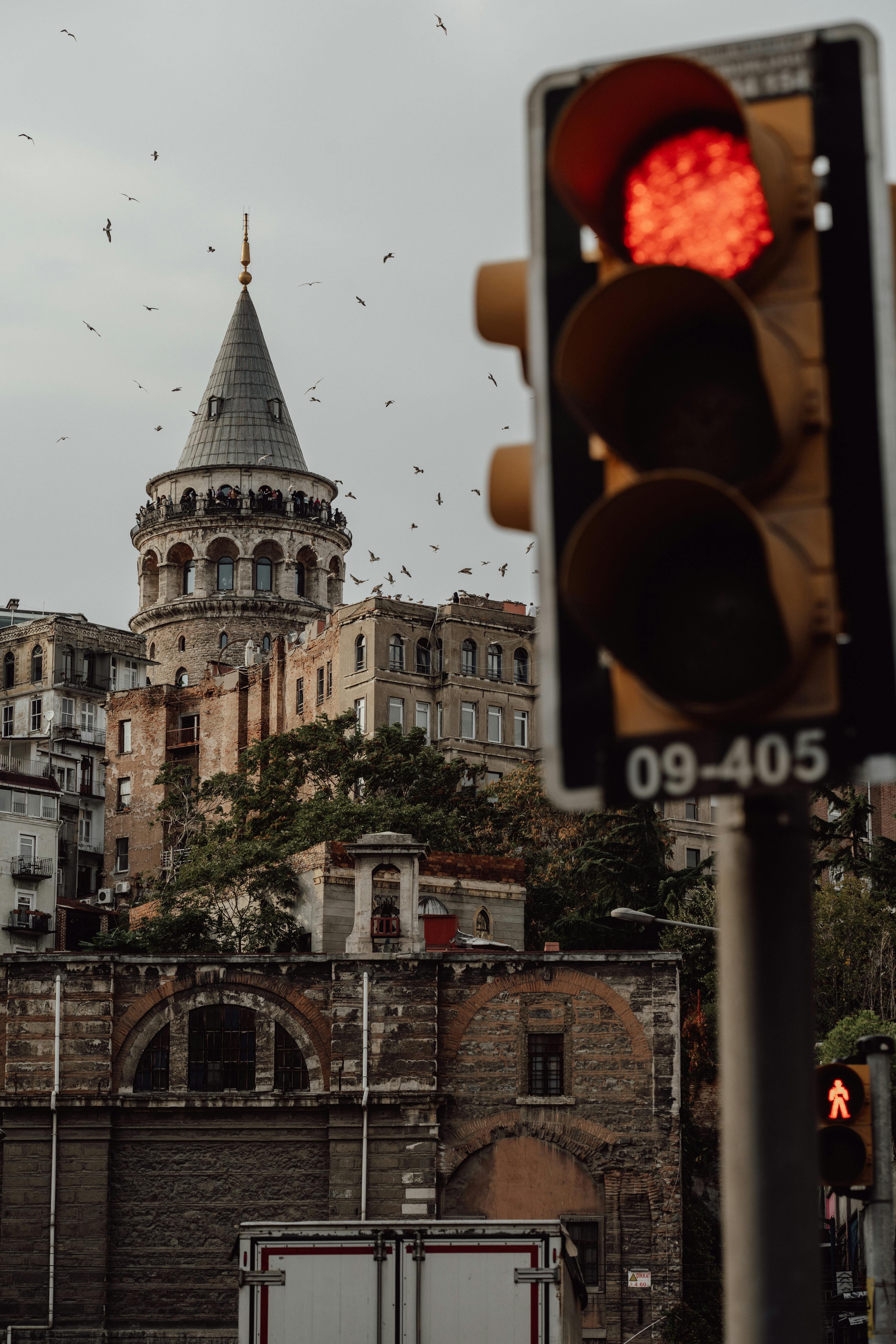View of Galata Tower in Istanbul with a red traffic light in the foreground, capturing urban atmosphere.