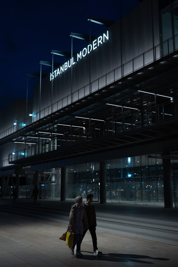 A Couple Walking On The Street During Night Time