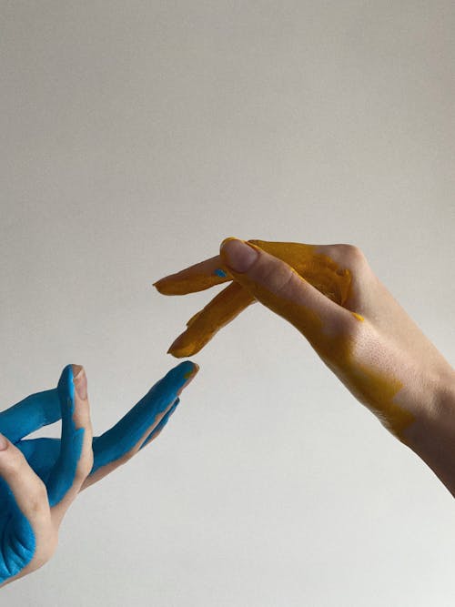 Close-up of a Hand with Blue Paint Touching a Hand with Yellow Paint 