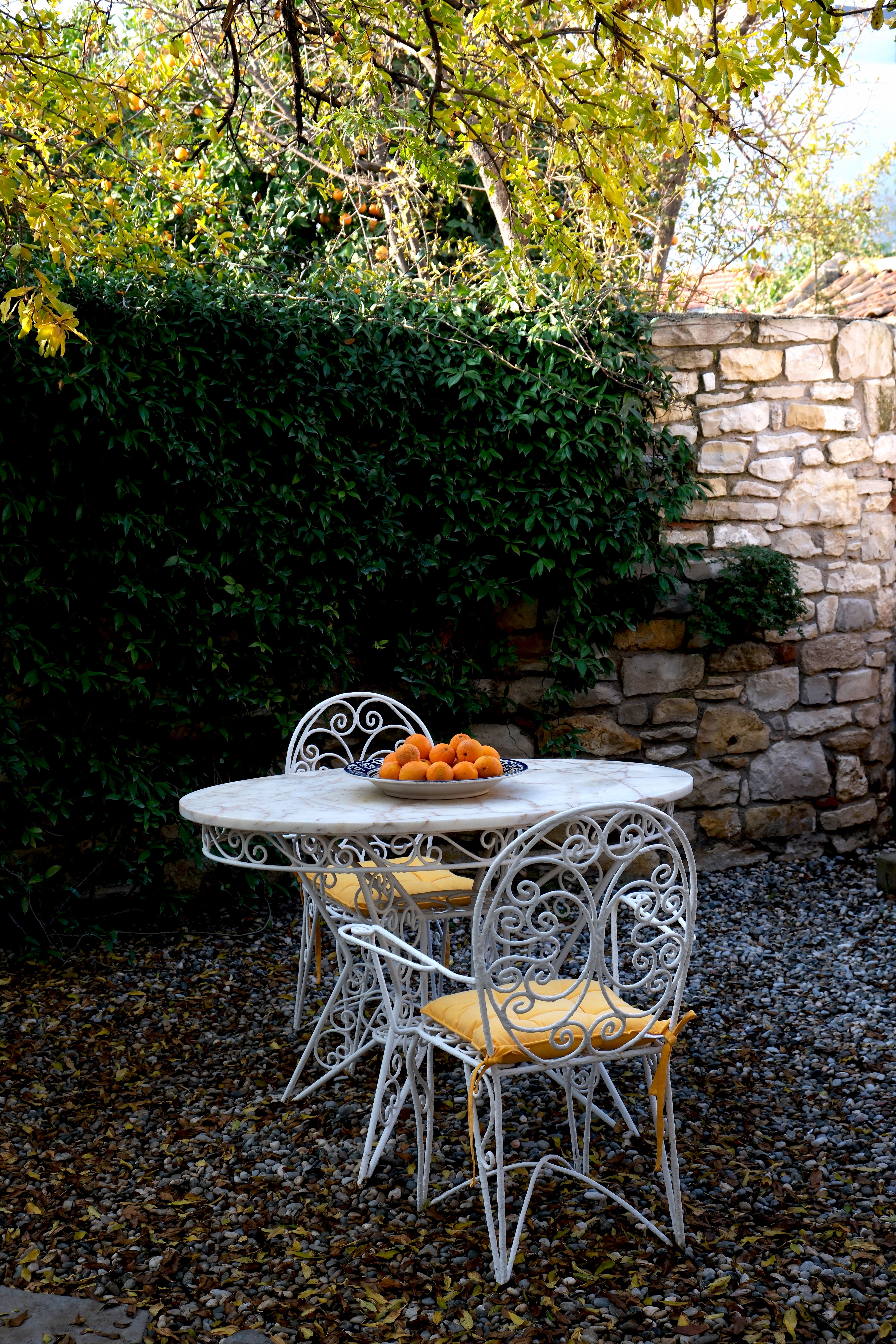 Elegant iron chairs around a white table with a bowl of oranges on a scenic patio.