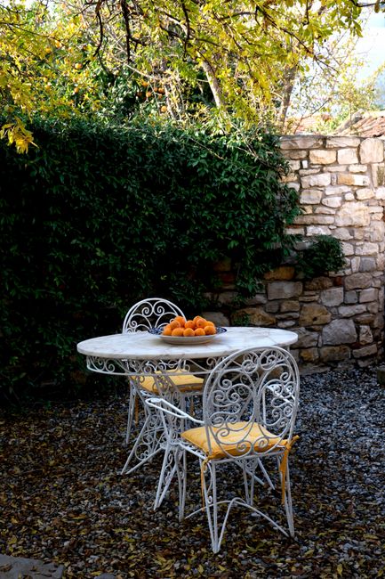 Elegant iron chairs around a white table with a bowl of oranges on a scenic patio.