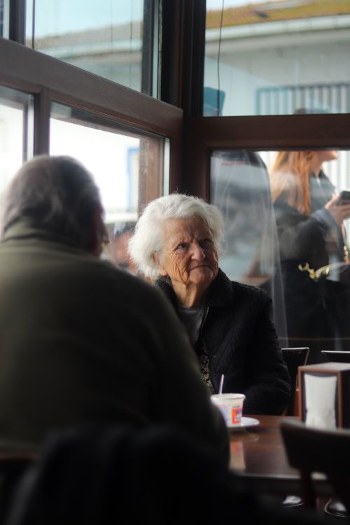 Free Senior woman with white hair sitting by a cafe window, enjoying a peaceful moment. Stock Photo